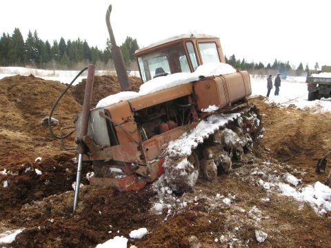 1987 Ford Bronco - A tracked tractor is stuck in a muddy, snowy area. Two people are visible in the background near a truck.