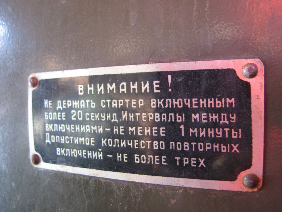 Black metal plate with white Russian text about starter limits, attached to a grey surface