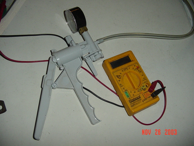 Hand vacuum pump with gauge and yellow digital multimeter on a workbench