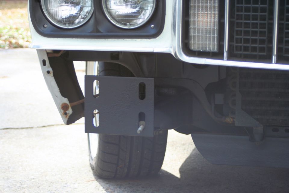 White vehicle's front bumper bracket attached to the frame, with a tire visible