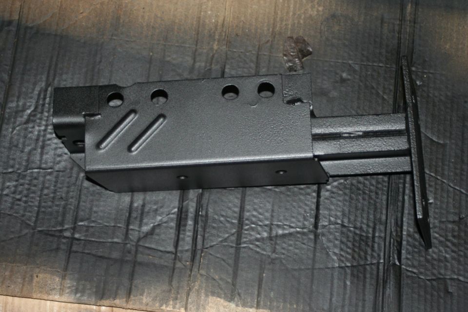 Black metal part with holes and angled indentations, possibly a frame component