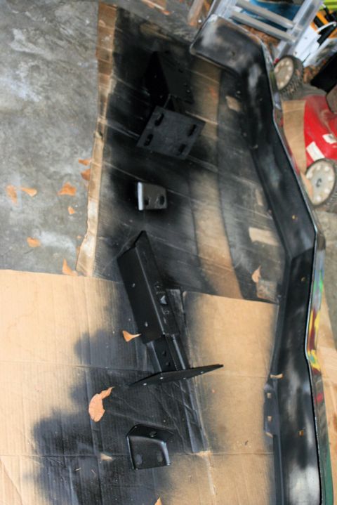 1976 Ford Ranchero - Car bumper and mounting hardware are laid out on cardboard, possibly for painting or repair.