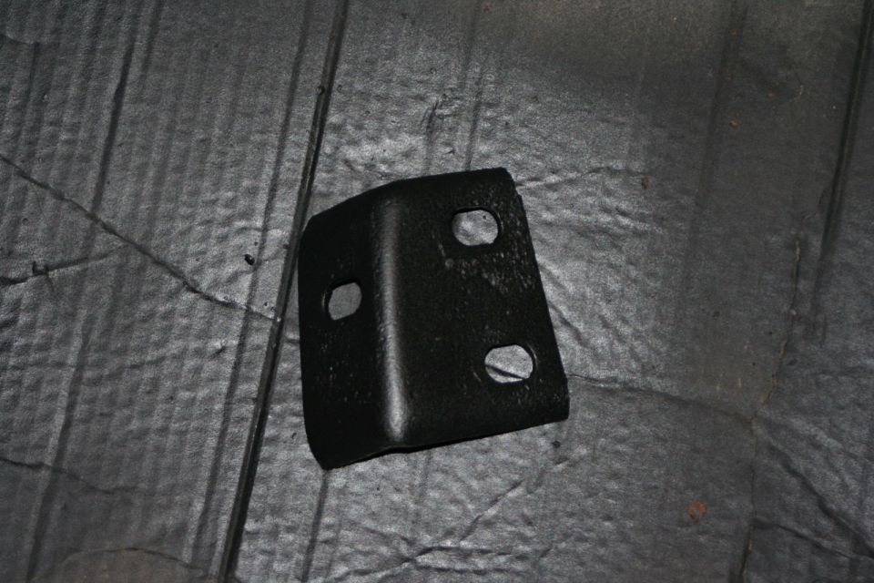black metal bracket with four holes, sitting on a textured gray surface