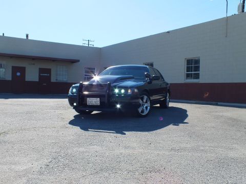 2003 Ford Crown Victoria - A black 2003 Ford Crown Victoria is parked in front of a building, a push bar and an aftermarket hood.