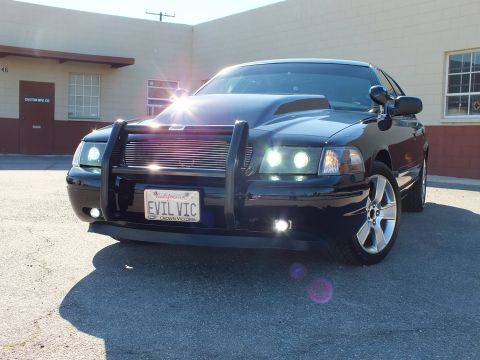 2003 Ford Crown Victoria - Front view of a modified Crown Victoria, halo projectors lit, EVIL VIC plate, chrome wheels on asphalt.