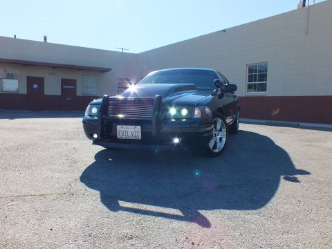 2003 Ford Crown Victoria - Front three-quarter view of a custom Crown Victoria, EVIL VIC plate, chrome wheels casting a long shadow.