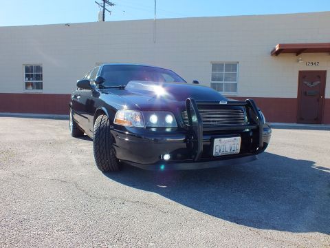 2003 Ford Crown Victoria - Low-angle front shot of a custom Crown Victoria with billet grille and chrome wheel on a paved lot.