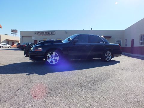 2003 Ford Crown Victoria - Side profile of a lowered black Crown Victoria with chrome wheels in an industrial parking lot.