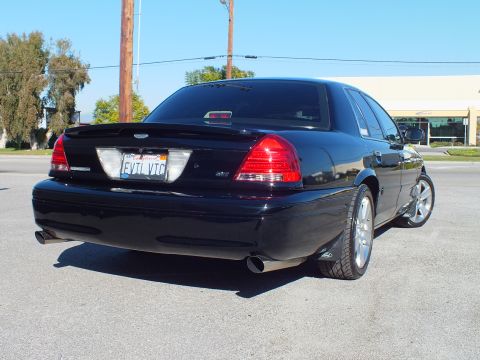 2003 Ford Crown Victoria - Rear view of a custom Crown Victoria with spoiler and chrome wheels in a sunny paved lot.