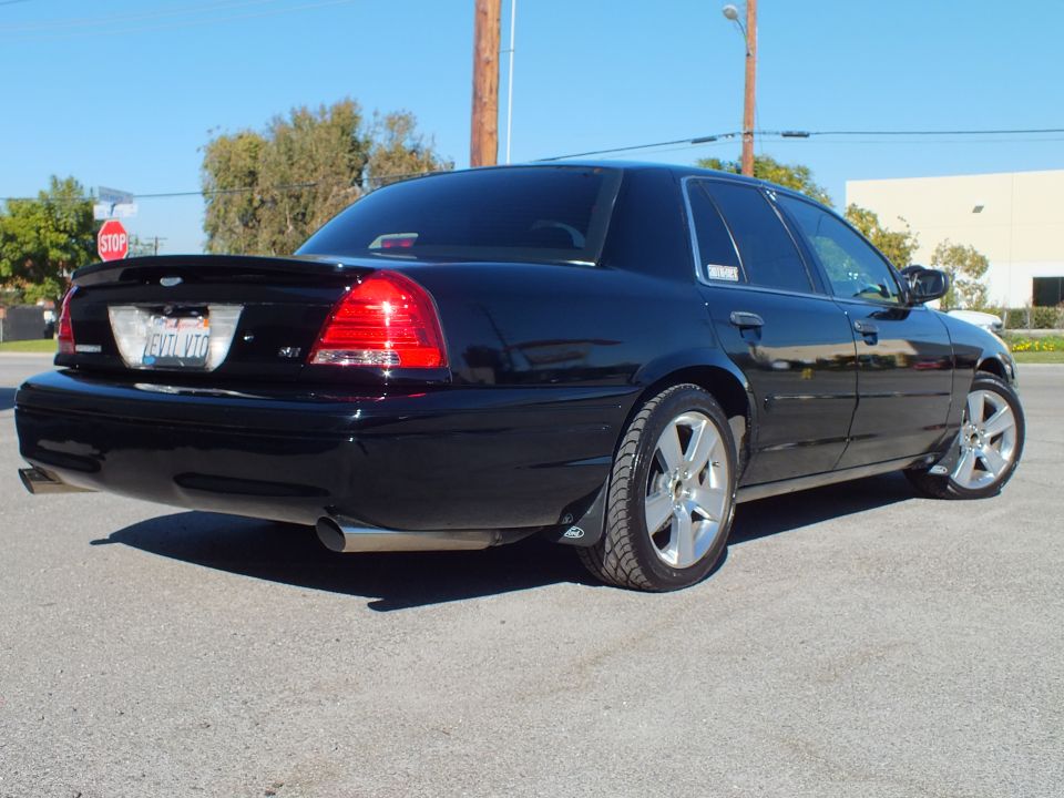 Black Ford Crown Victoria rear view with spoiler and chrome wheels near a stop sign