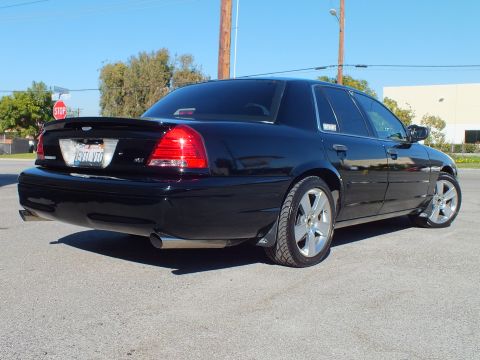 2003 Ford Crown Victoria - Rear quarter of a blacked-out Crown Victoria sedan with trunk spoiler, dual exhaust and chrome rims in a paved lot
