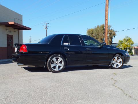 2003 Ford Crown Victoria - Side profile of a lowered black sedan, trunk spoiler and chrome rims, beside a building with power lines overhead