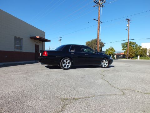 2003 Ford Crown Victoria - Distant rear-quarter shot of a black sedan with spoiler and chrome wheels in an empty paved lot