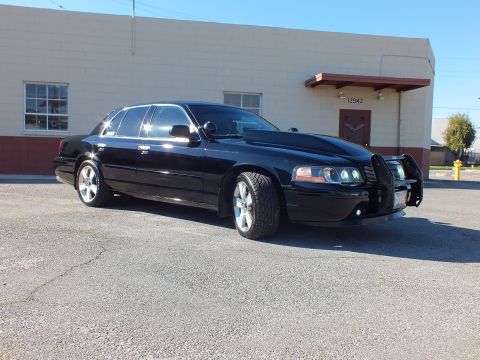 2003 Ford Crown Victoria - Front-quarter view of a black sedan fitted with a grille guard and billet grille on cracked asphalt