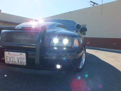 2003 Ford Crown Victoria - Sun-flared low-angle front shot of a black sedan, grille guard and EVIL VIC Crown Victoria plate