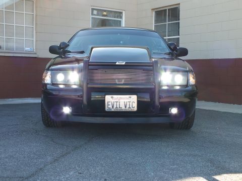 2003 Ford Crown Victoria - Front-facing black sedan with push bar, billet grille and lit projector lights, EVIL VIC plate