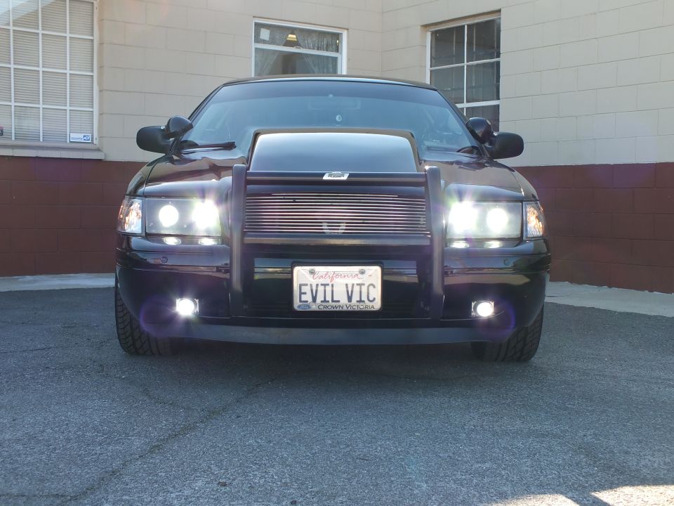 Black Crown Victoria head-on front view with grille guard, lit headlights and EVIL VIC plate