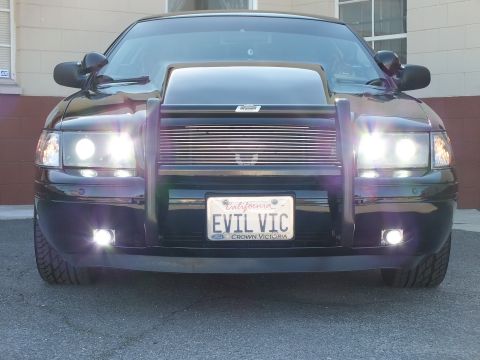 2003 Ford Crown Victoria - Head-on black sedan with push bar, billet grille and fog lights lit, EVIL VIC plate centered
