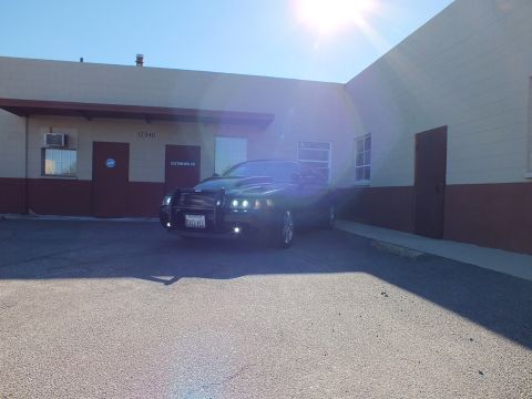 2003 Ford Crown Victoria - Black sedan with grille guard parked near a Custom Auto building, sun flare above the roofline