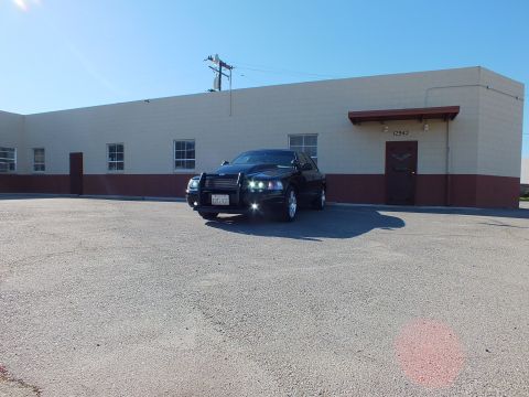 2003 Ford Crown Victoria - Distant front-quarter shot of a black sedan with grille guard against a low industrial building