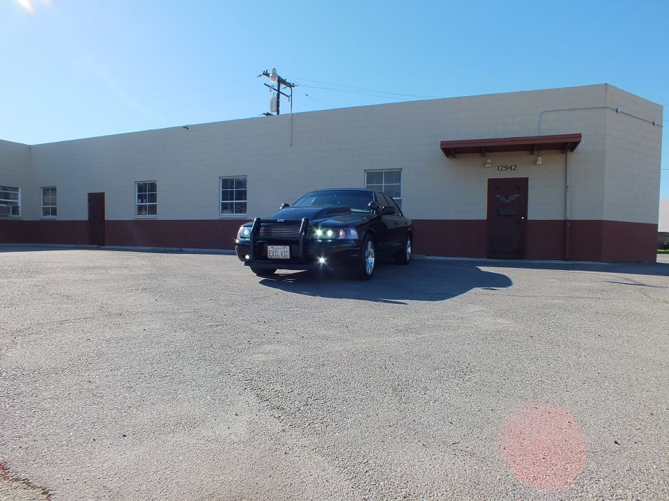 Black Crown Victoria front three-quarter parked by long building, grille guard and chrome wheels