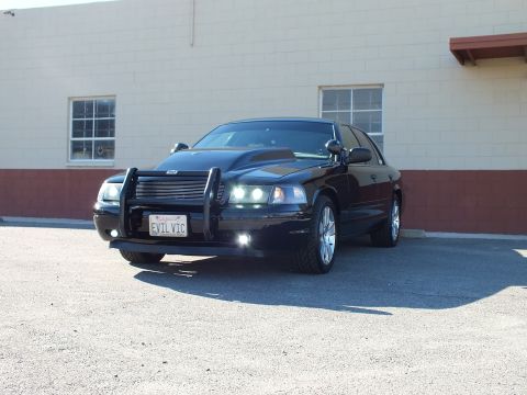 2003 Ford Crown Victoria - Black sedan angled front view, grille guard and chrome wheels, EVIL VIC plate visible up front