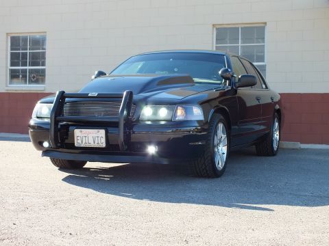 2003 Ford Crown Victoria - Front-quarter view of a black sedan with grille guard and lit headlights, EVIL VIC California plate