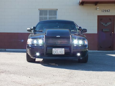 2003 Ford Crown Victoria - Head-on black sedan with billet grille and grille guard, lit projector lights, EVIL VIC plate