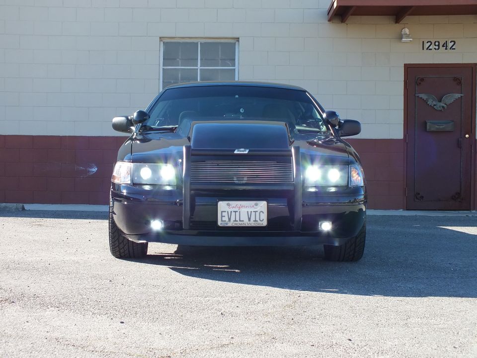 Black Crown Victoria front view with grille guard, lit headlights and EVIL VIC California plate