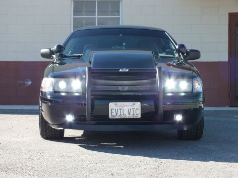 2003 Ford Crown Victoria - Front-facing black sedan with scooped hood, billet grille and grille guard, EVIL VIC plate
