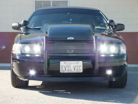 2003 Ford Crown Victoria - Head-on black sedan with grille guard and lit projectors, EVIL VIC Crown Victoria plate