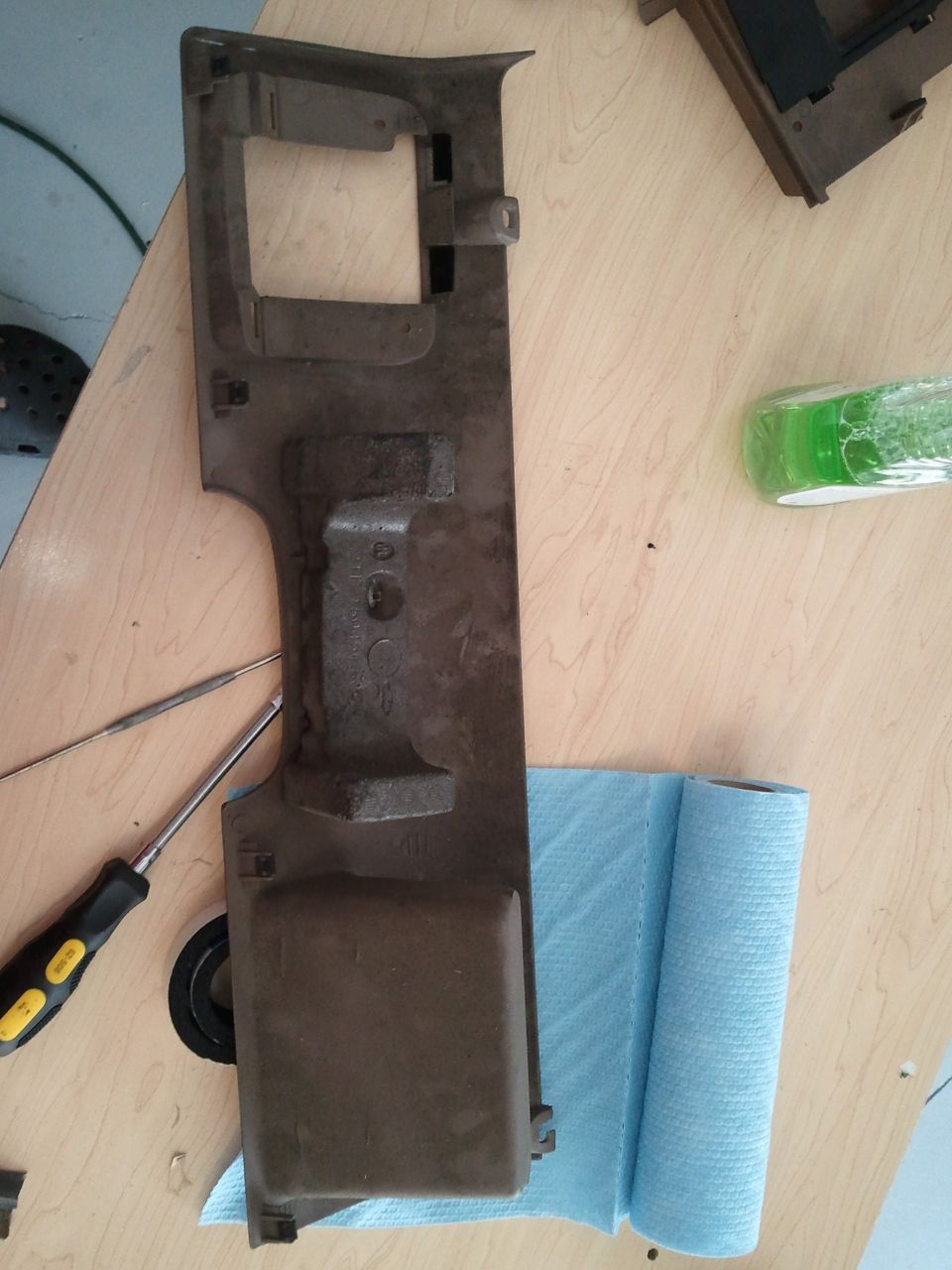 Brown plastic interior trim piece on a wooden surface with a screwdriver and pick tool