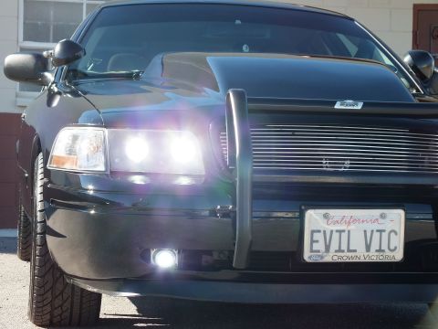 2003 Ford Crown Victoria - Angled front shot of a black sedan with lit headlights, billet grille and a Crown Victoria license plate frame.