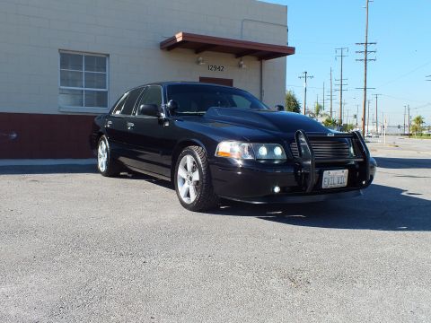2003 Ford Crown Victoria - Black sedan parked at a front three-quarter angle beside a building, push bar and polished wheels visible.