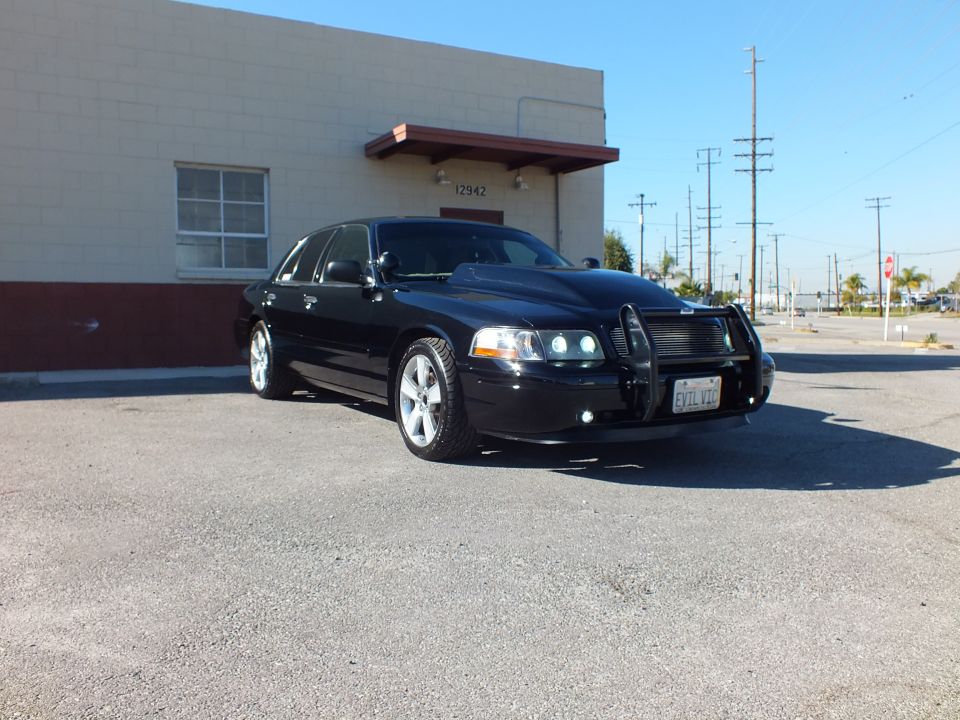 Black Ford Crown Victoria front three-quarter view parked beside building with push bar