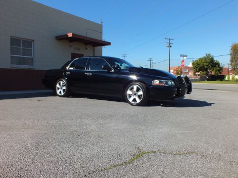 2003 Ford Crown Victoria - Side-front view of a black lowered sedan on polished wheels parked in an empty lot near a building.