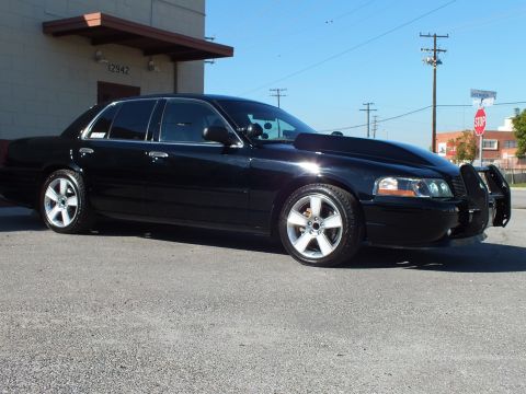 2003 Ford Crown Victoria - Full driver-side profile of a black lowered sedan with polished wheels, stop sign visible behind.