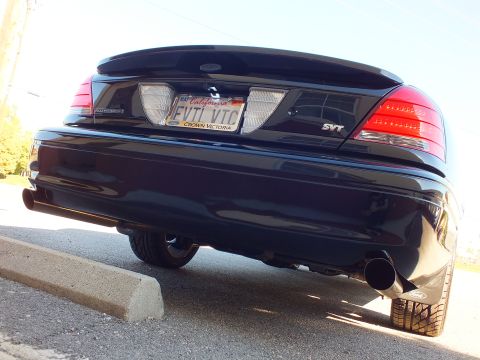 2003 Ford Crown Victoria - Ground-level rear shot of a black sedan, SVT badge and California EVIL VIC plate, twin exhaust outlets.