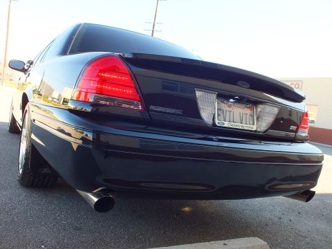 2003 Ford Crown Victoria - Rear-quarter low shot of a black sedan, SVT badge, EVIL VIC plate and red LED taillight detail.