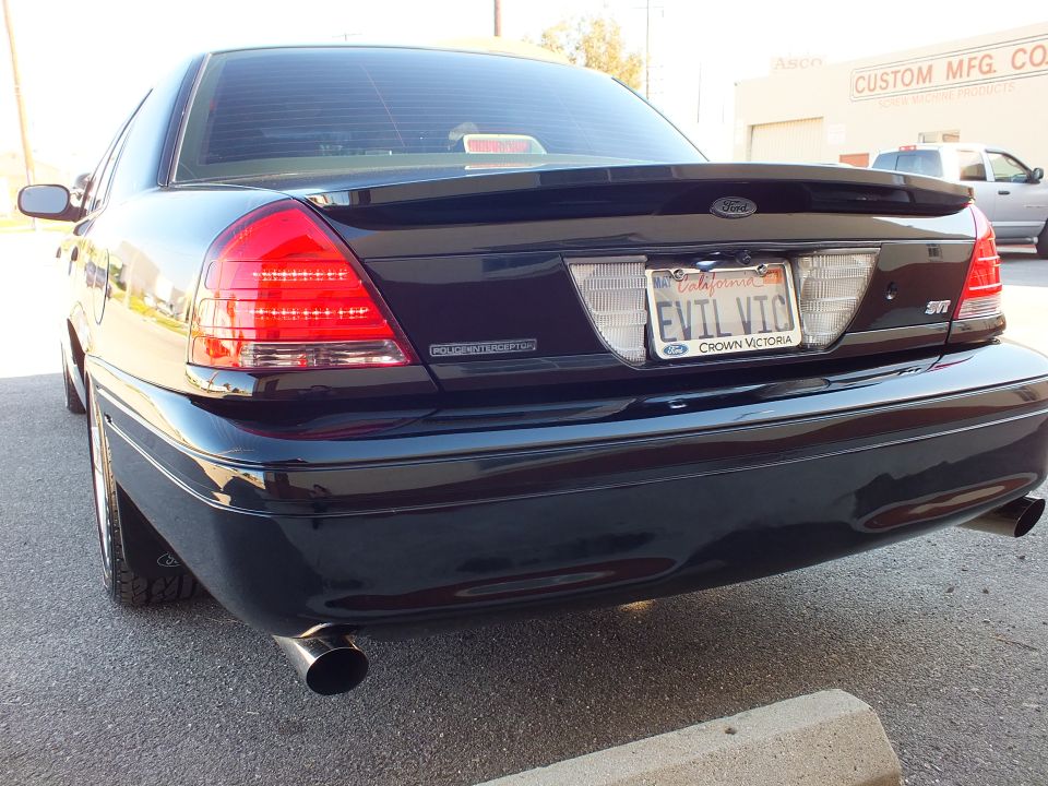 Rear of black Ford Crown Victoria, EVIL VIC plate and Custom Mfg building behind