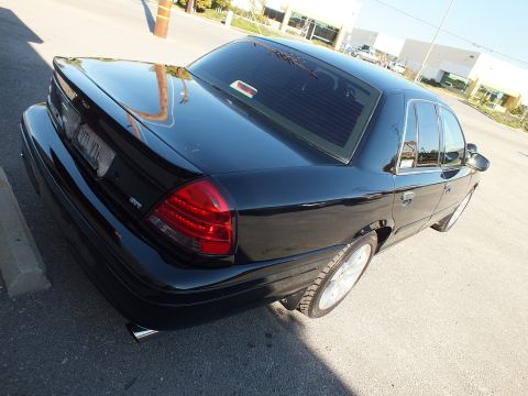 2003 Ford Crown Victoria - Elevated rear-quarter view of a black lowered sedan on polished wheels, taillights and SVT badge visible.