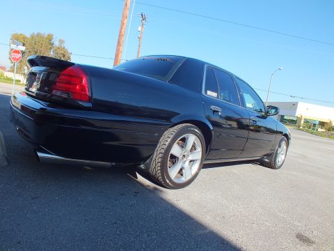 2003 Ford Crown Victoria - Low rear-quarter angle of a black lowered sedan on polished wheels, stop sign and poles behind.
