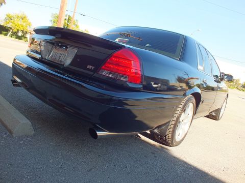 2003 Ford Crown Victoria - Low rear-quarter shot of a black sedan, SVT badge, single exhaust tip and polished wheels near a curb.