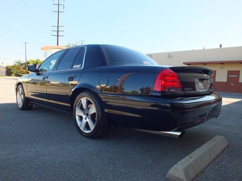 2003 Ford Crown Victoria - Rear quarter of a lowered black Crown Victoria sedan showing trunk spoiler, red taillights and polished five-spoke wheel.