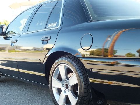 2003 Ford Crown Victoria - Tight shot of a black sedan's rear door, fuel filler door and polished wheel with Ford center cap.