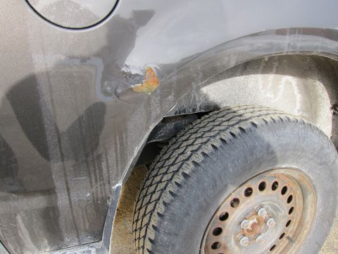1991 Ford Crown Victoria LTD - Close-up of a gray car's rear quarter panel showing a rust spot and a tire. The vehicle appears to be in need of repair.