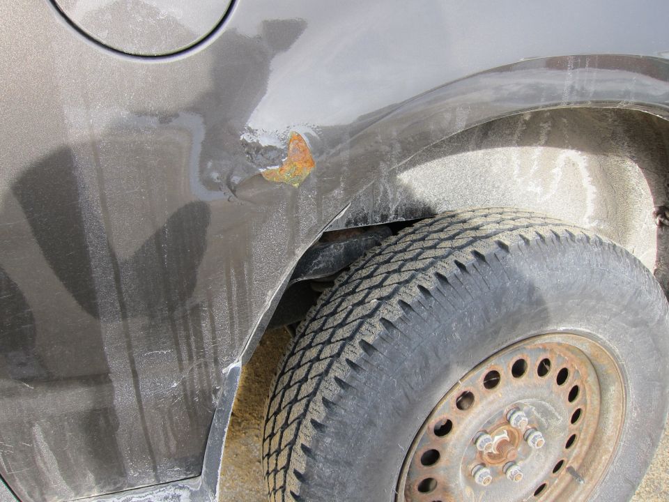 Gray car rear quarter panel with rust spot and tire