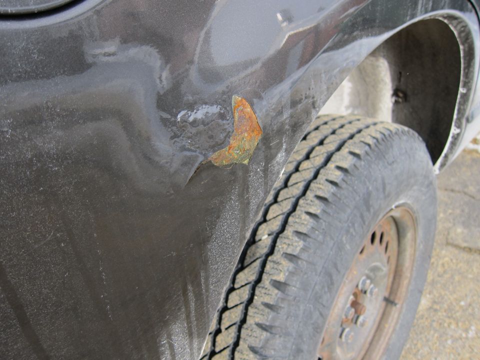 Close-up of rust forming on a dark-colored car fender near the wheel well