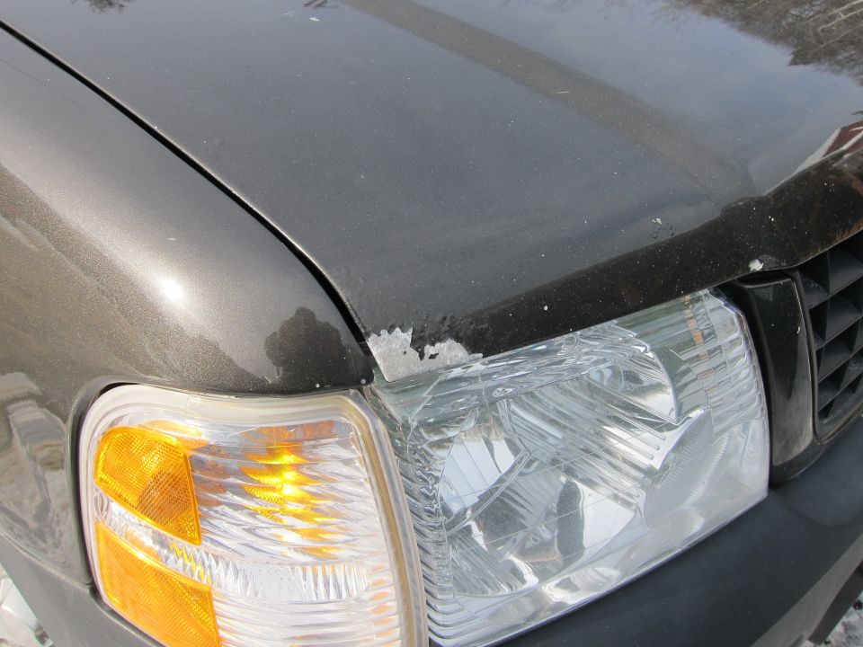 Dark gray car hood with peeling paint near the headlight and grille