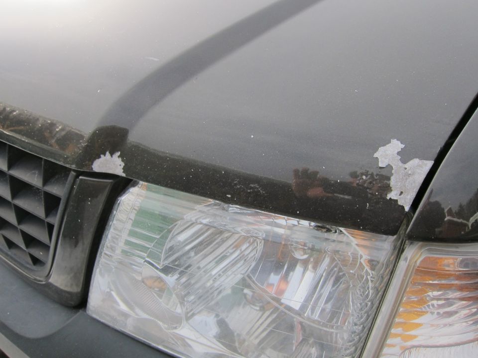 Dark SUV hood with peeling paint and clear headlight